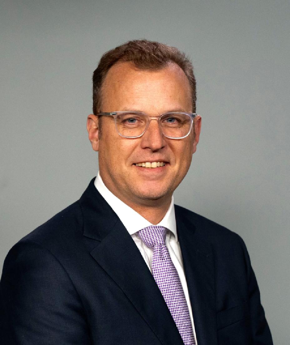 Eric smiling from the chest up in a suit against a gray background.
