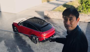 A man standing on a balcony overlooking the 2027 INFINITI QX65 in the daytime.