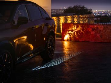 Angled view of the 2027 INFINITI QX65 at nighttime, an INFINITI lighting sequence is illuminated on the ground.