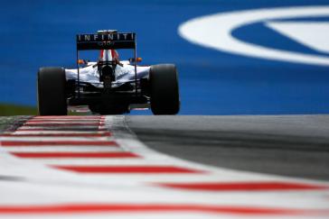 Back of a Formula One car driving on the red and white striped side of the track .