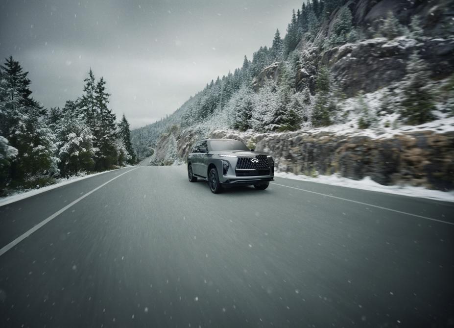 Un INFINITI QX80 gris 2026 roulant sur une route hivernale sous la neige.