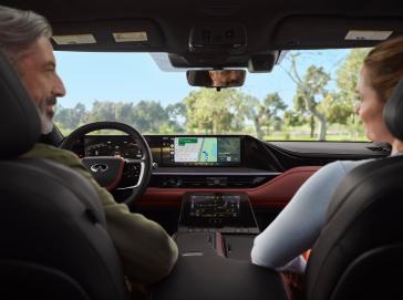 Vista interior del INFINITI QX80 Autograph desde la segunda fila, mostrando la consola central con pantalla táctil, controles digitales y detalles en cuero y metal, reflejando lujo y conectividad en carretera.