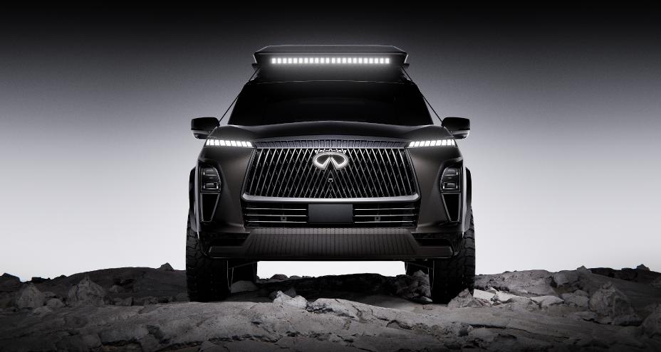 Front view of the INFINITI QX80 Terrain Spec parked on rocky terrain, the headlights and emblem are illuminated.