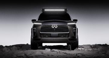 Front view of the INFINITI QX80 Terrain Spec parked on rocky terrain, the headlights and emblem are illuminated.