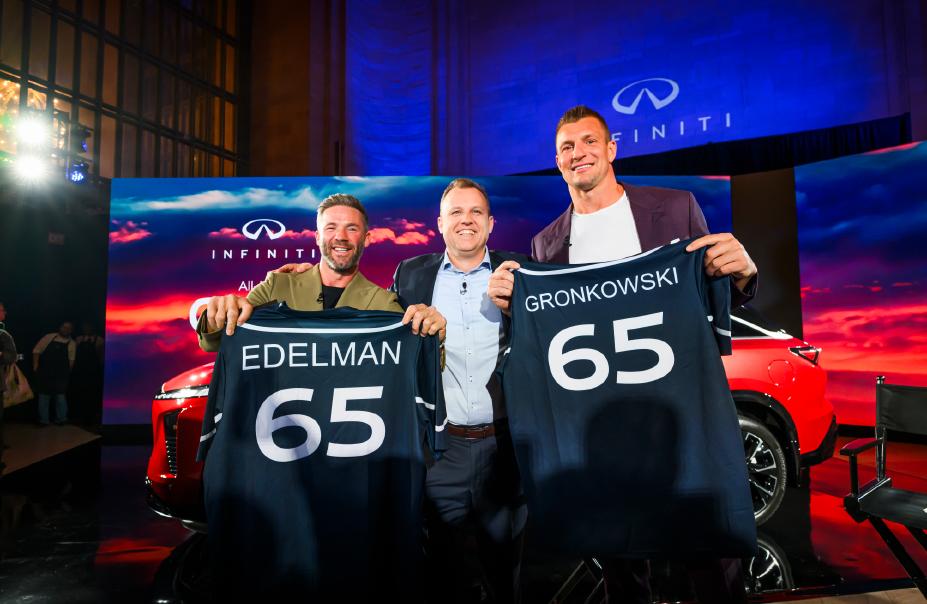 Two sports stars pose with another man, they hold up jerseys with their name and "65" displayed on the back.