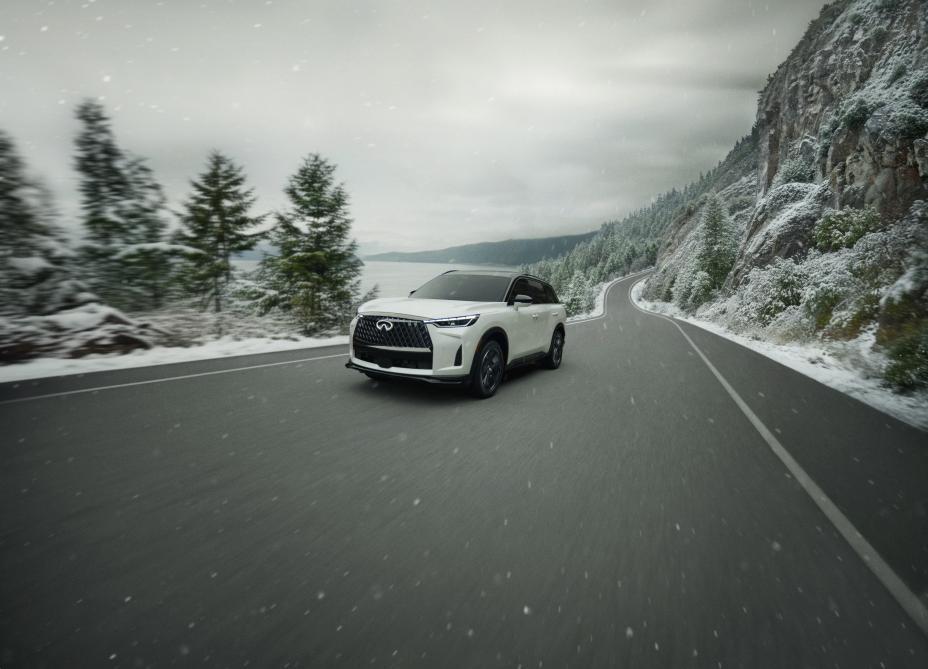 Un INFINITI QX60 blanc 2026 roulant sur une route hivernale sous la neige.