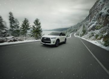 Un INFINITI QX60 blanc 2026 roulant sur une route hivernale sous la neige.