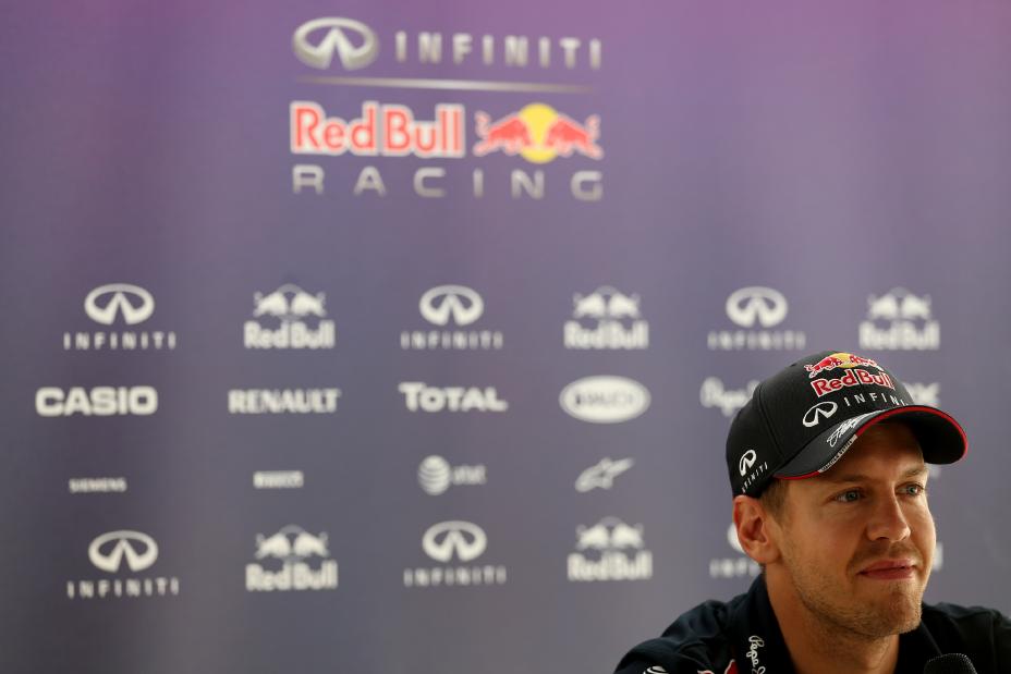 An F1 driver wearing a hat with the RedBull logo banner in the background