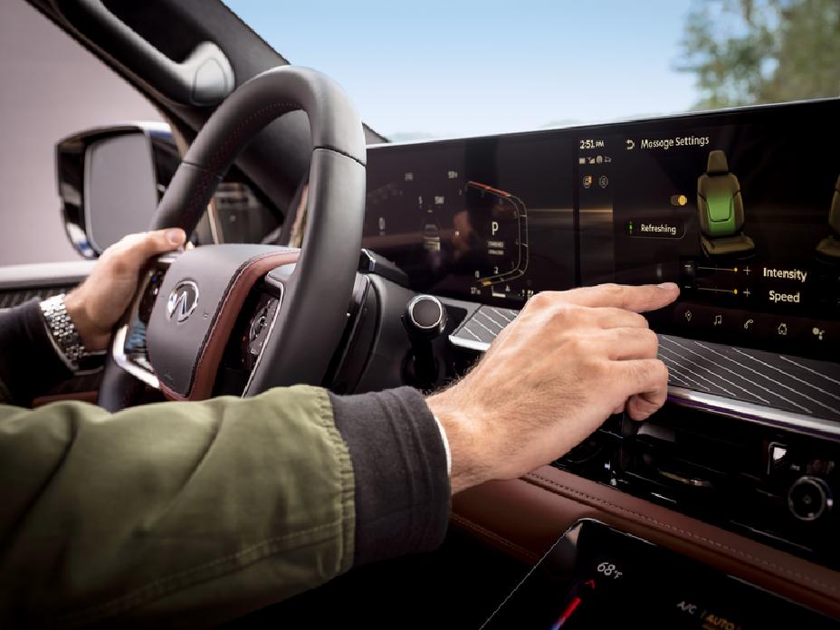 Vista interior de un vehículo INFINITI desde el asiento del conductor, mostrando el volante, pantallas digitales y acabados premium mientras se observa el exterior a través del parabrisas.