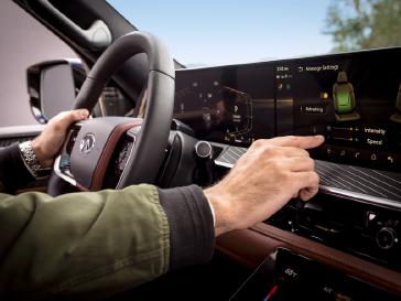 Vista interior de un vehículo INFINITI desde el asiento del conductor, mostrando el volante, pantallas digitales y acabados premium mientras se observa el exterior a través del parabrisas.