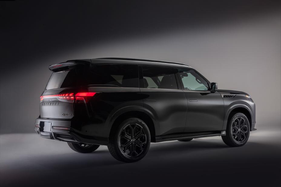 Rear and side view of the 2026 INFINITI QX80 SUV in black, with illuminated taillights and a sculpted body design; the vehicle is displayed in a studio setting with lighting that emphasizes its contours.