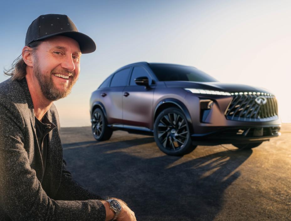 A man smiling crouched in front of the QX65 Monograph, the sun beams on one side.