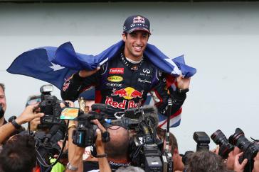 A man surrounded by cameras with a blue flag draped over his shoulders