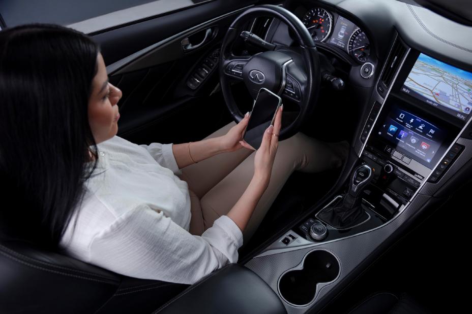 INVITADA INFINITI dentro de un vehículo utilizando su celular para agendar una cita en línea, reflejando la integración perfecta entre conectividad inteligente y comodidad premium.