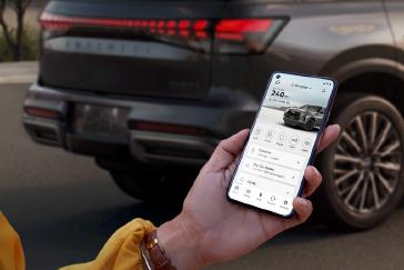 Persona sosteniendo un smartphone que muestra la app MiINFINITI mientras una SUV INFINITI está estacionada al fondo.