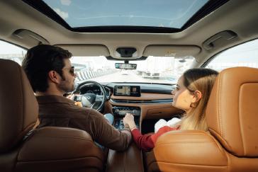 Pareja disfrutando un trayecto cómodo y relajado dentro de una INFINITI QX60, tomada desde los asientos traseros durante una experiencia de INFINITI Membership Experience