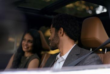 Close up de una pareja conversando y sonriendo dentro de la cabina de una INFINITI QX60, destacando la cercanía, el confort y la atmósfera íntima del interior del vehículo.