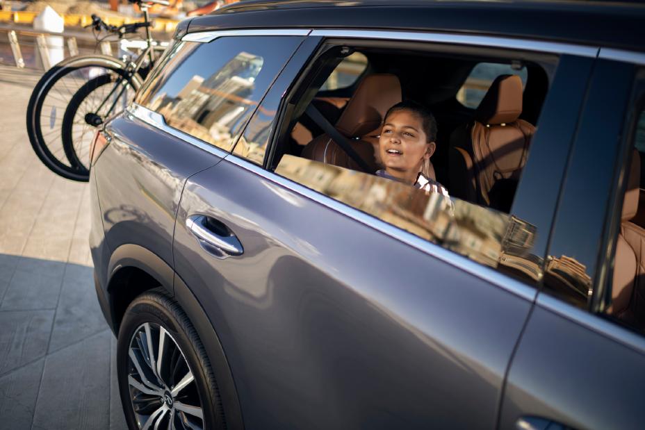 Niña sentada en el asiento trasero de una INFINITI QX60, con cinturón de seguridad puesto, en un interior espacioso y elegante que refleja confort y protección.