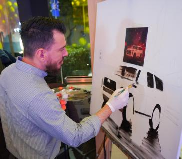 Artista pintando un cuadro del INFINITI QX80 Autograph 2026 durante la inauguración de INFINITI Universidad, destacando la conexión entre creatividad y lujo.