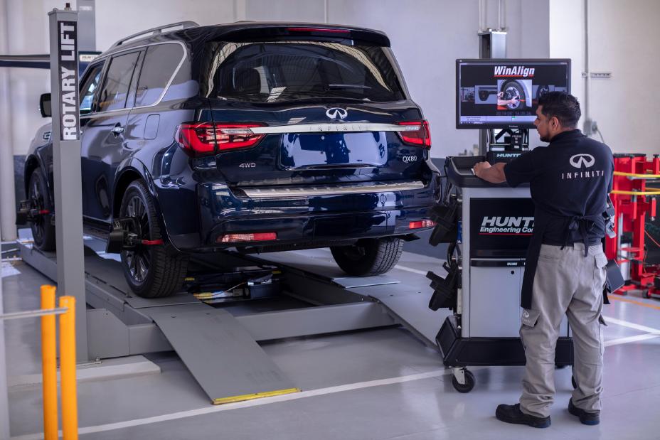 Técnico especializado INFINITI ajustando la alineación de las llantas de un QX80, mostrando el cuidado profesional y la tecnología aplicada para garantizar estabilidad y confort en la conducción.