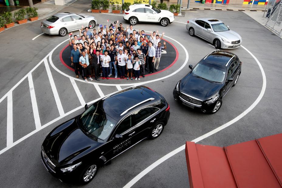 Five Infiniti cars making a half circle and a group of people posing for a photo.