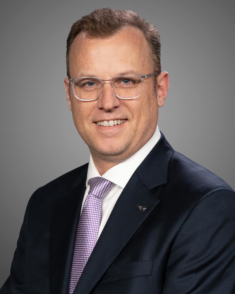 Eric smiling from the chest up in a suit against a gray background.