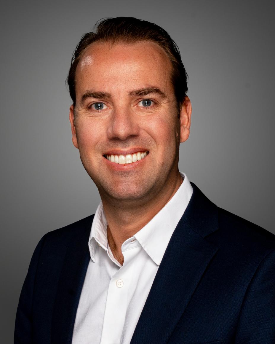 Tiago smiling from the chest up against a gray background.