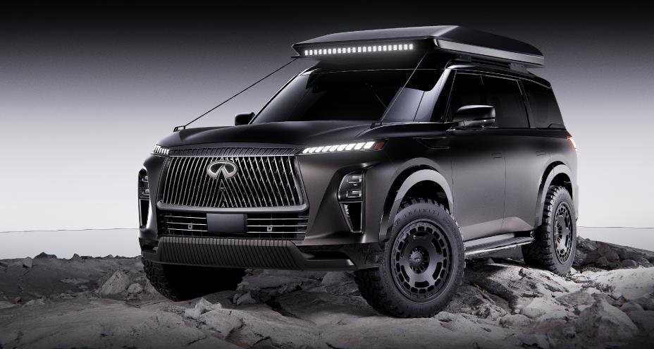 Right 3/4 view of the INFINITI QX80 Terrain Spec parked on rocky terrain, the headlights are illuminated.