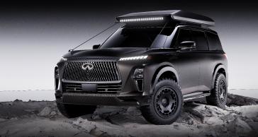 Right 3/4 view of the INFINITI QX80 Terrain Spec parked on rocky terrain, the headlights are illuminated.
