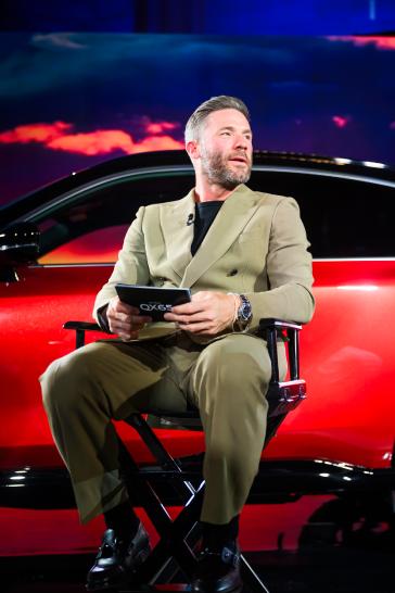 Julian Edelman sits in front of the 2027 INFINITI QX65 in a tan suit.
