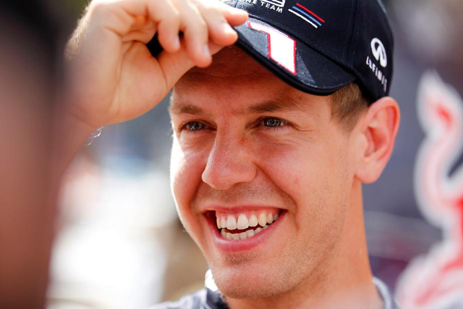 A headshot of Sebastian Vettel smiling and holding the brim of his cap