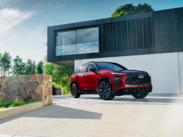Front right 3/4 view of the 2027 INFINITI QX65 parked in front of a modern building in the daytime.