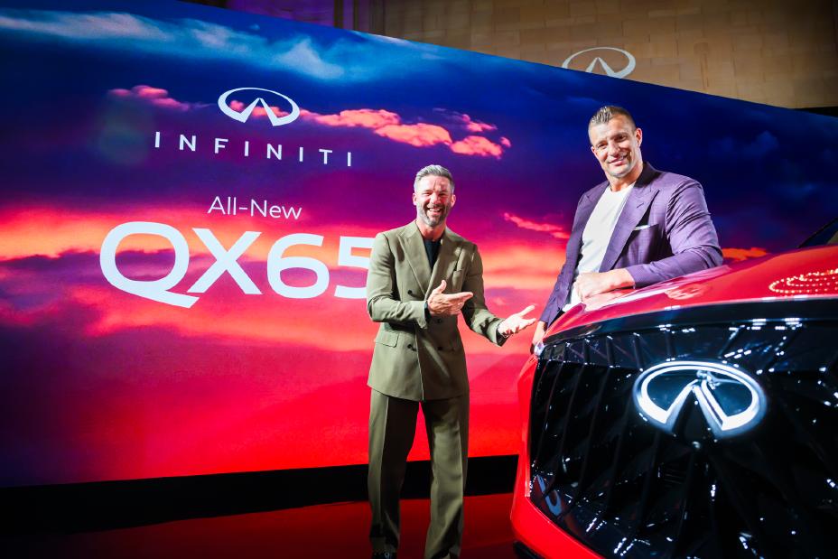 Two men post near the 2027 INFINITI QX65 with a stage size display screen behind.