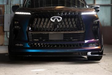 Close up of the front fascia on the INFINTI QX80 R-Spec build, the headlights and emblem are illuminated.
