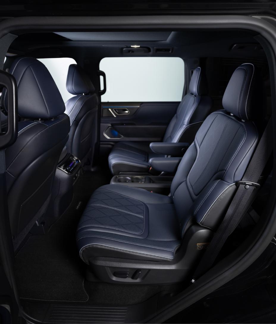 Interior view of the 2026 INFINITI QX80, showing the second row with two individual dark blue leather seats featuring armrests, headrests, and visible stitching. The image is taken from the open side door, with black carpeting visible on the floor.