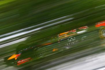 Blurry photo looking through the tress at a F1 car.