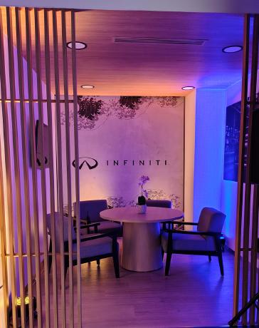 Vista desde el exterior de la sala de recepción INFINITI Universidad, diseñada bajo el concepto Omotenashi, con iluminación cálida, materiales premium (madera, cuero, metal), tecnología LED avanzada.
