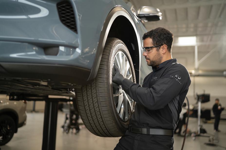 Técnico de INFINITI revisando la llanta de un vehículo en un entorno profesional, destacando la atención experta del programa INFINITI Protect.