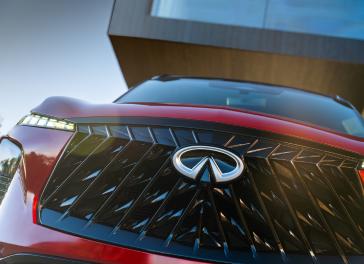 Close up of the grill on the 2027 INFINITI QX65, sunlight reflects off the Sunfire red paint.
